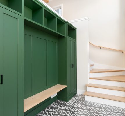 A large foyer with a vibrant green storage unit, white oak bench and stairs, and a black and white pattern tile flooring.